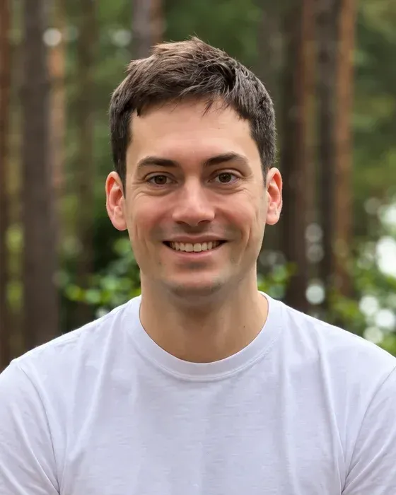 Tom Bennet, smiling, in a pine wood